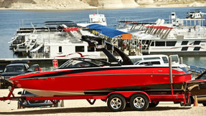 A red boat on a trailer near a marina, resting on bunk board padding that keeps the hull stable and safe during transport